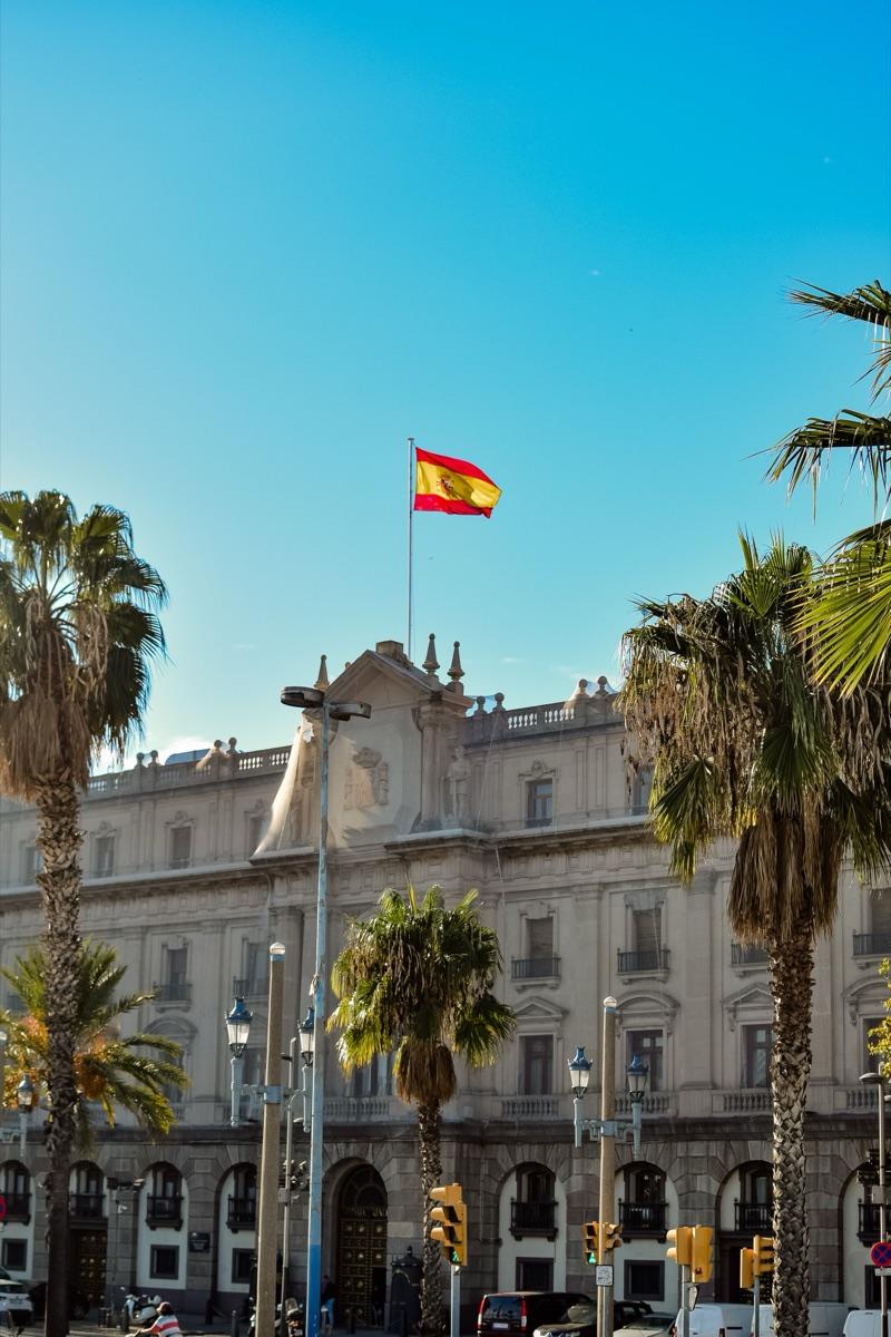 Bandera de España ondeando sobre un edificio histórico con palmeras