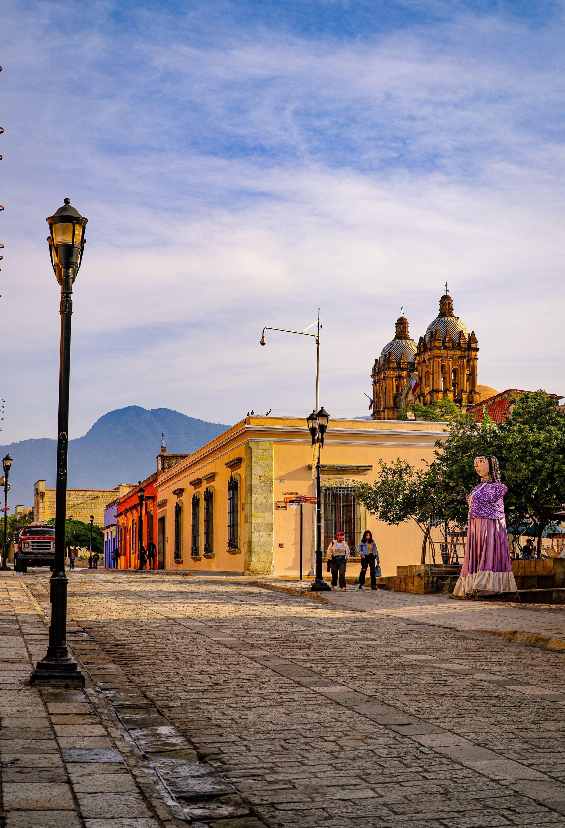 Calle empedrada de Oaxaca, México, con el templo de Santo Domingo al fondo y una mojiganga