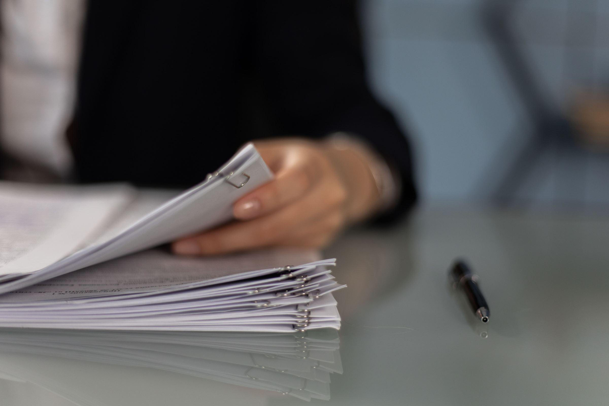 Persona revisando un fajo de documentos sobre una mesa