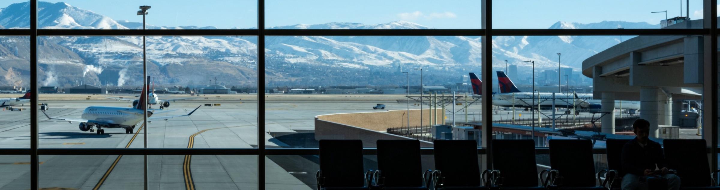 Sala de espera de un aeropuerto con aviones en la pista y montañas nevadas al fondo